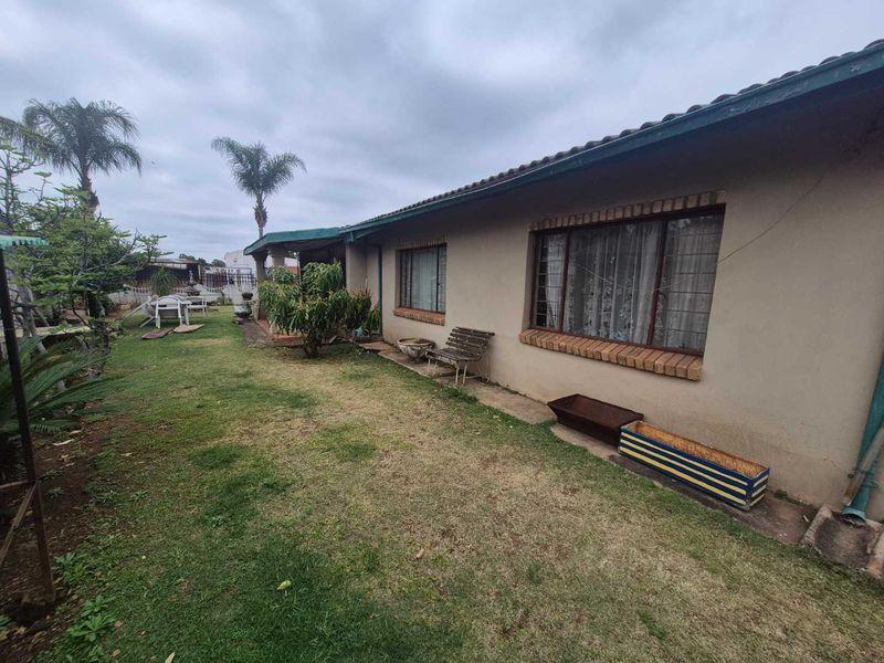 Rear view of the house featuring a lawn area, tiled roof, and windows with security bars.