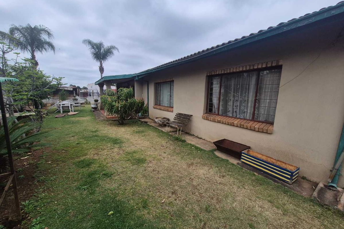 Rear view of the house featuring a lawn area, tiled roof, and windows with security bars.