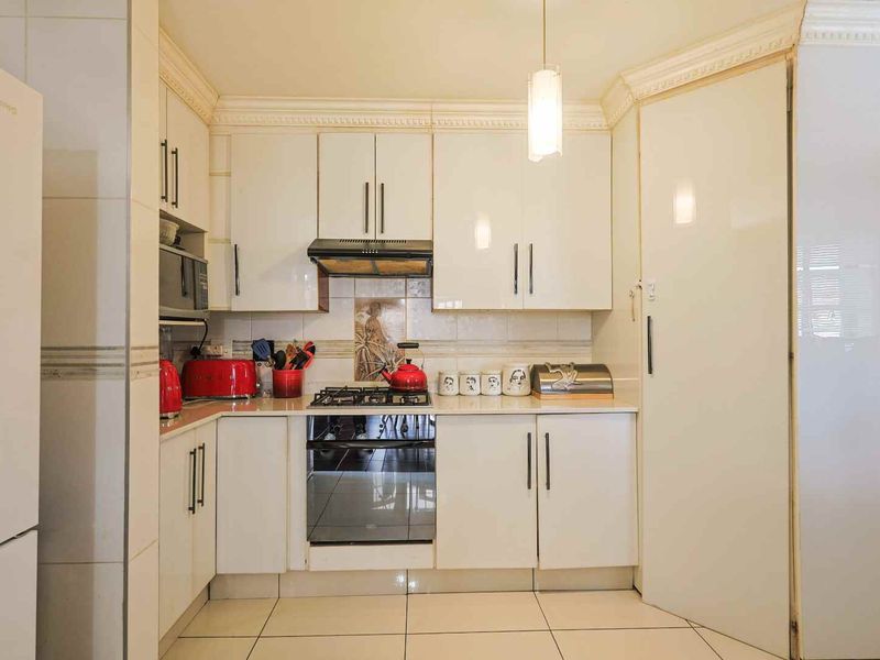A compact kitchen featuring white high-gloss cabinetry, a gas hob with an integrated extractor fan, and tiled flooring throughout.