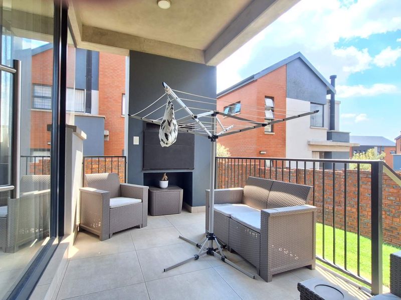 A covered patio featuring tiled flooring, a built-in braai, and a metal balustrade, providing a functional outdoor entertainment space.