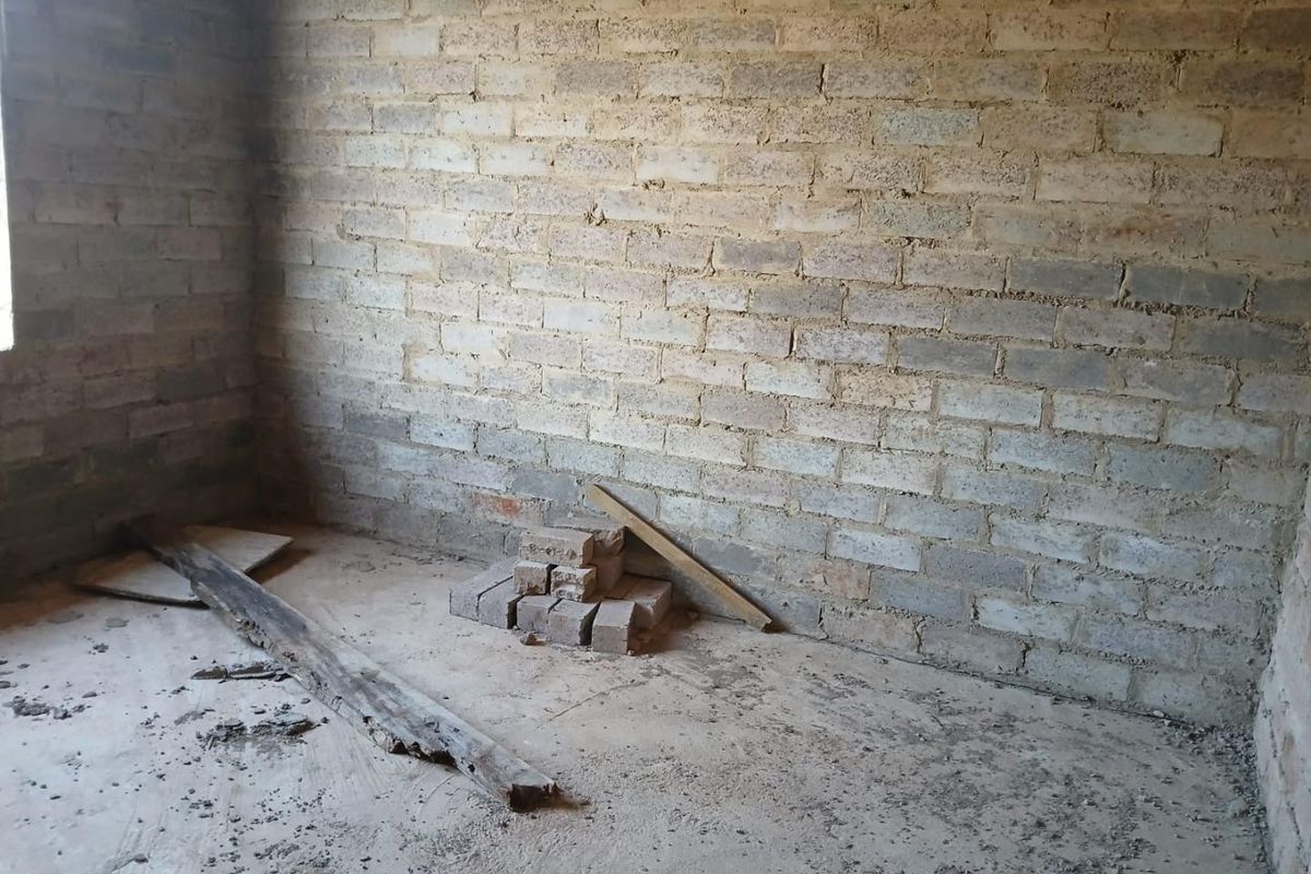 An unfinished room featuring exposed brick walls and a raw concrete floor, offering a blank canvas for renovation and interior finishing.