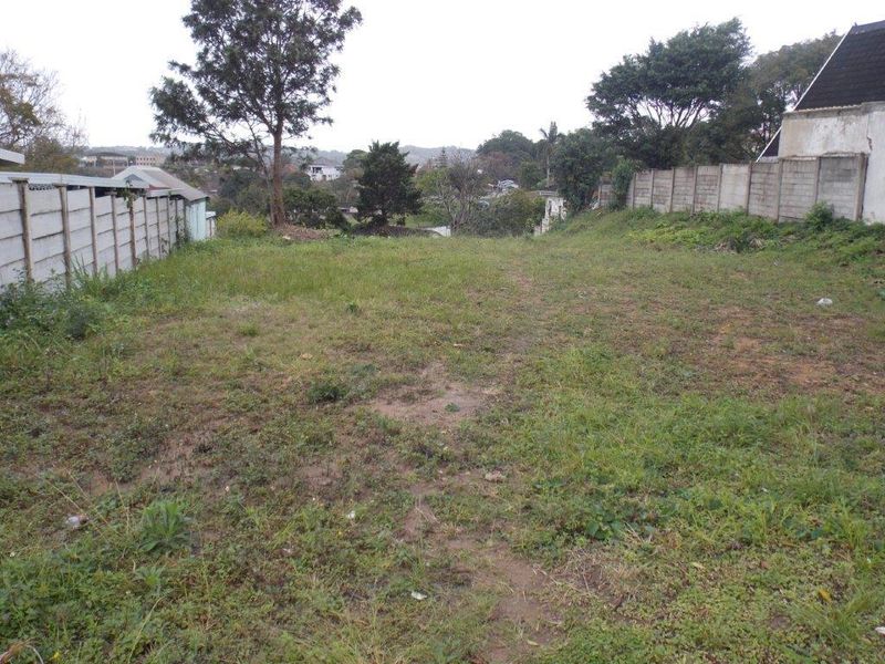 A vacant residential plot featuring a grassed surface and enclosed by precast concrete boundary walls on both sides.