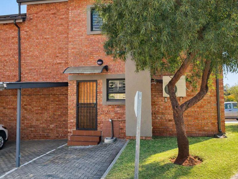 Front elevation of a face-brick townhouse featuring a paved driveway, carport, and secure entrance.