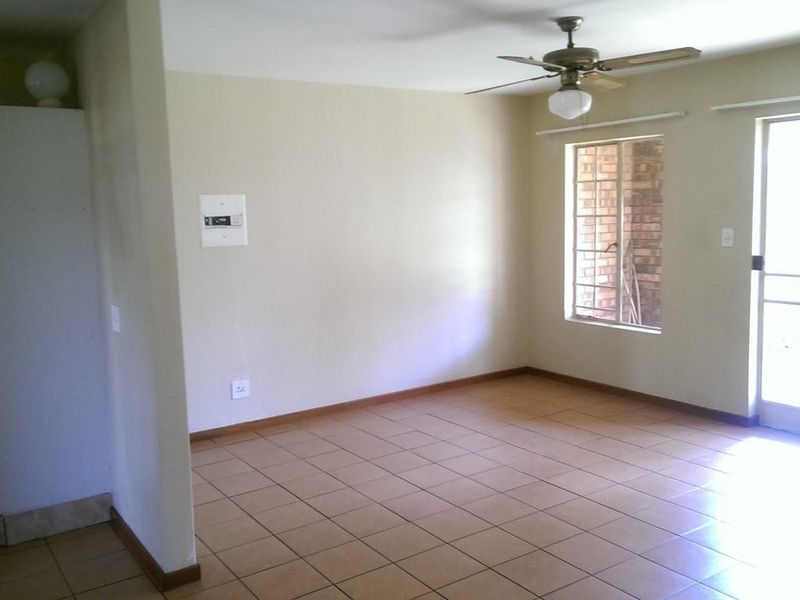 An empty living area featuring tiled flooring, a ceiling fan, and direct access to an outdoor space through a security gate.