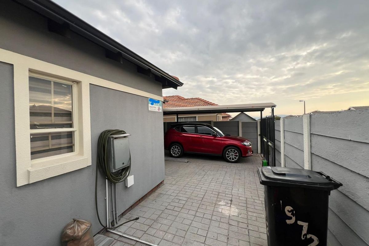 A paved side yard area featuring a carport structure and precast concrete boundary walling.