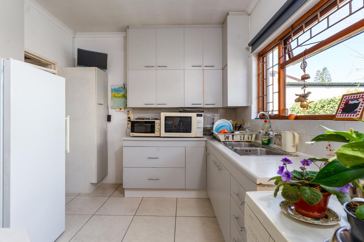 A functional kitchen featuring white cabinetry, tiled flooring, a double stainless steel sink, and a window providing natural light.