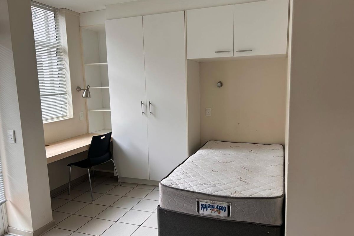A functional bedroom featuring built-in white cabinetry, overhead storage, and a integrated desk workspace with tiled flooring.