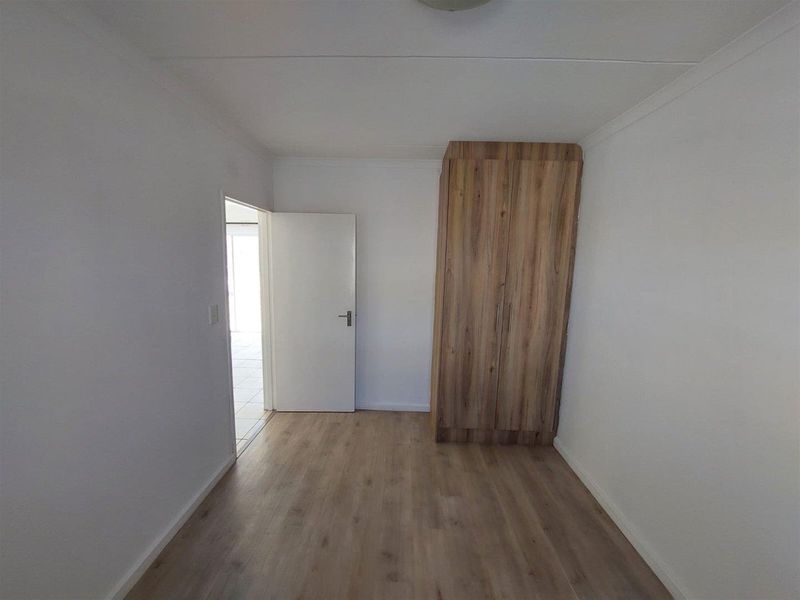 A clean, empty bedroom featuring light wood-look laminate flooring and a built-in wooden wardrobe, offering a neutral space ready for personalization.