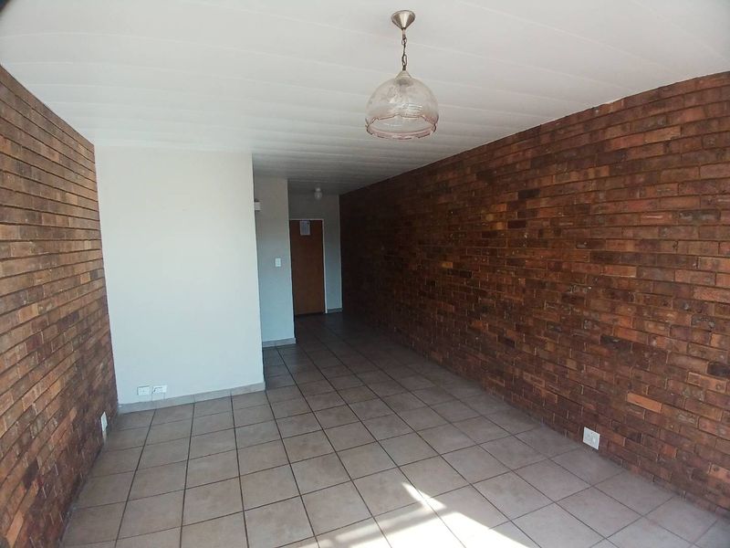 An empty living area featuring exposed brick walls, tiled flooring, and a central pendant light fixture, offering a blank canvas for renovation.