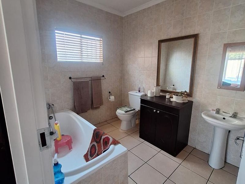 A functional bathroom featuring a built-in bathtub, pedestal washbasin, toilet, and vanity cabinet with neutral wall and floor tiling.