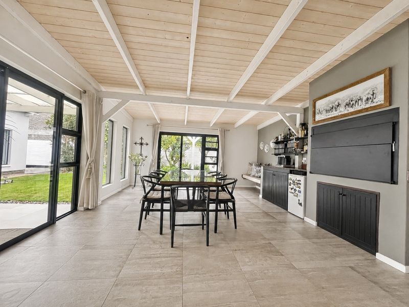 Spacious dining area featuring exposed timber beam ceilings, large glass sliding doors opening to the garden, and custom built-in cabinetry with a fireplace.