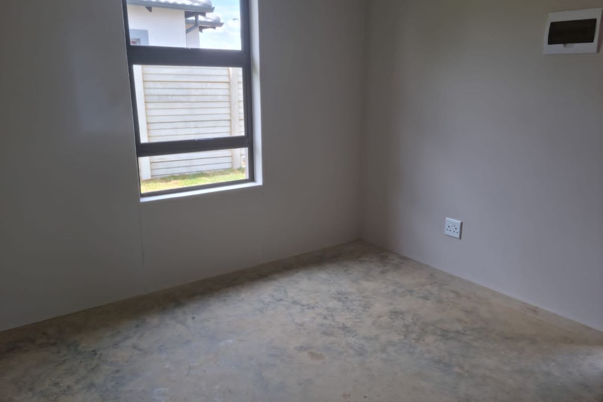 An empty bedroom featuring an aluminium window, electrical socket, and distribution board, with an unfinished concrete floor ready for final flooring installation.
