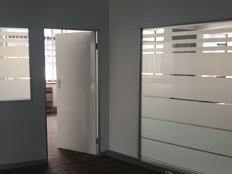 A clean, professional office space featuring modern frosted glass partitions, neutral wall finishes, and carpeted flooring, offering a bright and functional work environment.