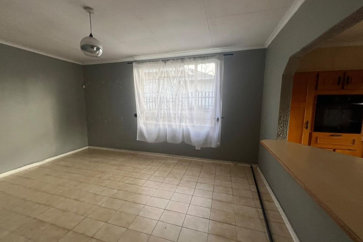 An empty living room featuring tiled flooring, a pendant light, and an arched opening leading to the kitchen area with a breakfast bar.