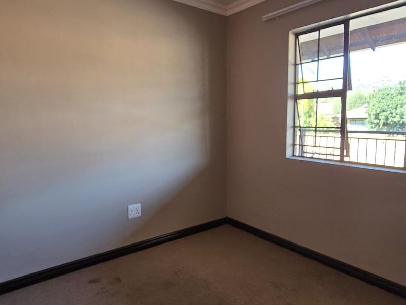 An empty bedroom featuring a built-in cupboard, carpeted flooring, and a metal-framed window with security bars.