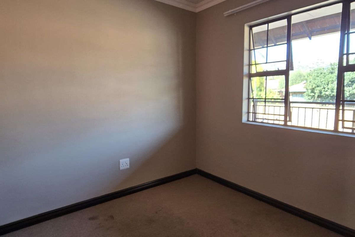 An empty bedroom featuring a built-in cupboard, carpeted flooring, and a metal-framed window with security bars.