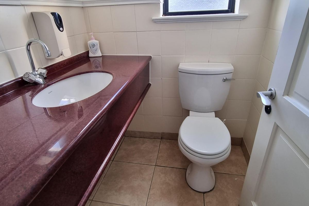 A functional office bathroom featuring a vanity with an integrated sink, tiled walls, and a standard toilet.