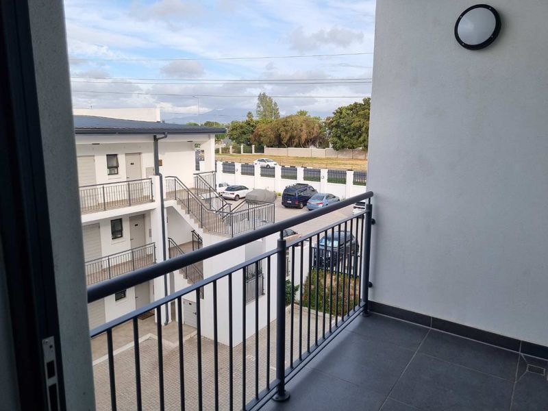 A clean, modern balcony featuring dark tiled flooring and a secure metal balustrade, overlooking the apartment complex parking area.