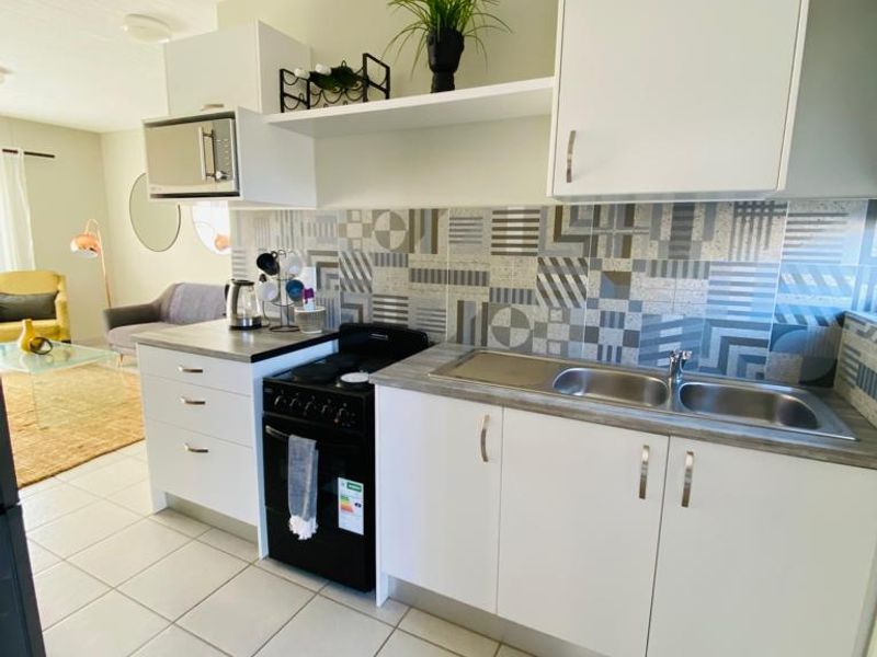 Open plan kitchen featuring white cabinetry, patterned tile backsplash, double stainless steel sink, and a freestanding stove, seamlessly flowing into the adjacent living area.