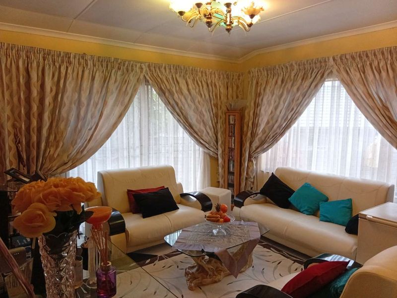 A comfortable living room featuring large windows with draped curtains and a central decorative ceiling light fixture.