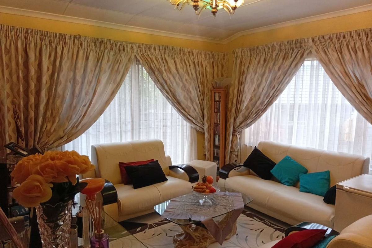 A comfortable living room featuring large windows with draped curtains and a central decorative ceiling light fixture.