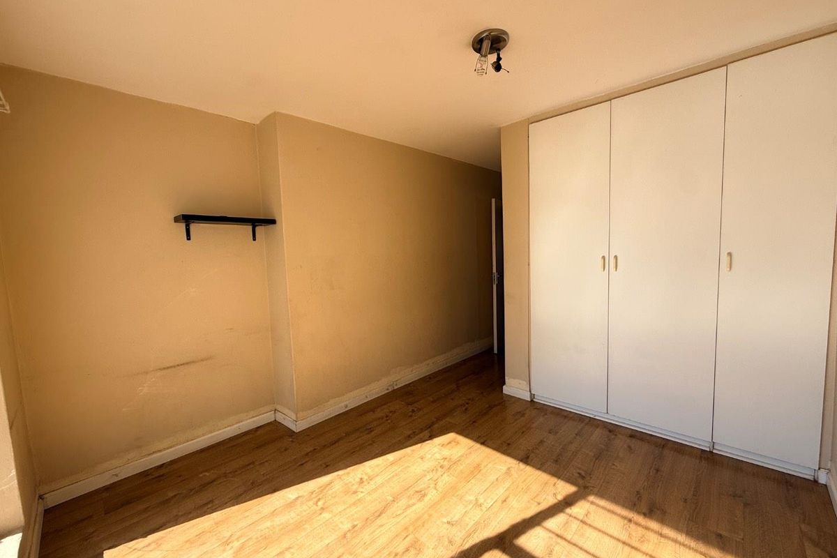 An empty bedroom featuring wood-look laminate flooring and built-in white wardrobes, offering a blank canvas for personalization.