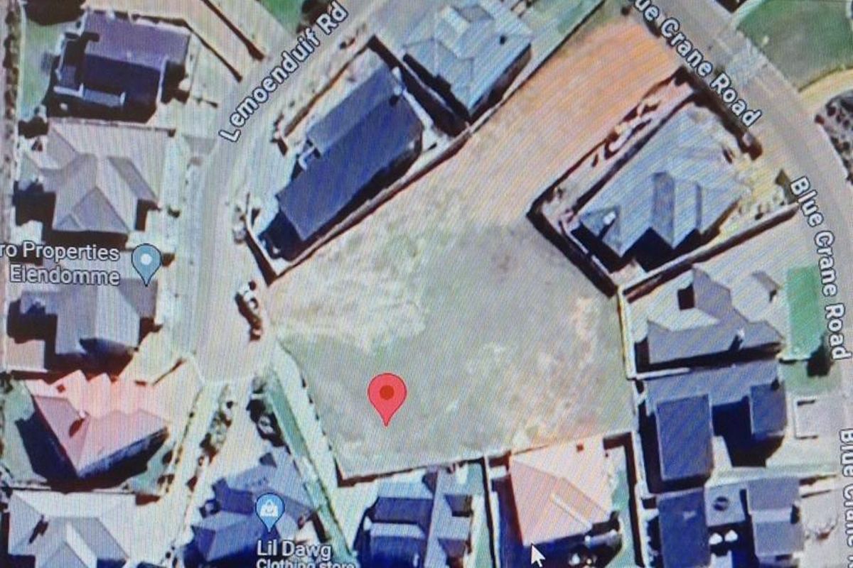 An aerial view of a vacant residential plot situated within a developed suburban neighborhood, showing surrounding properties and street access.