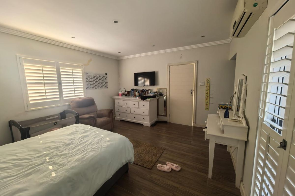 Spacious bedroom featuring laminate flooring, plantation shutters, and a wall-mounted air conditioning unit.