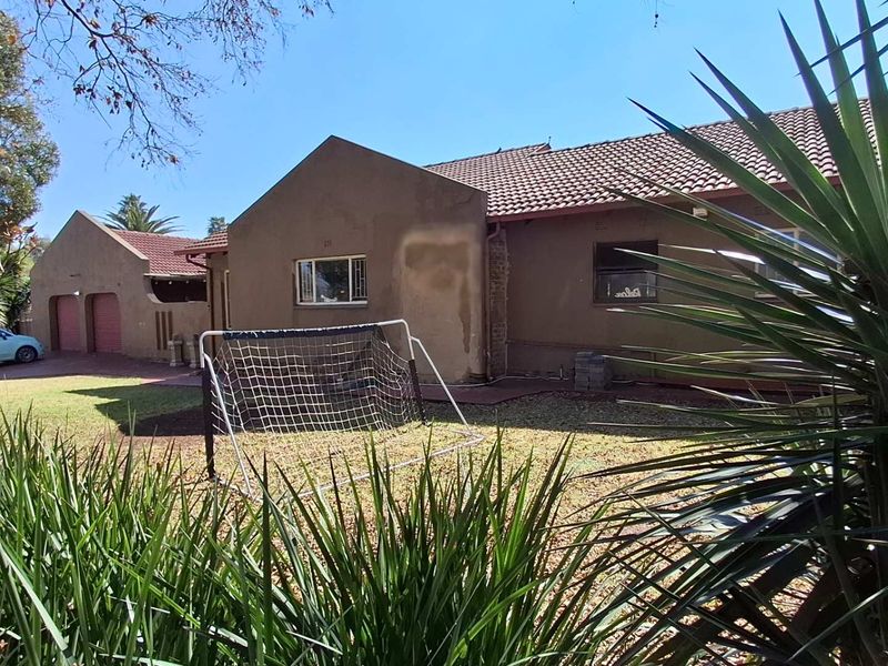 Rear view of the house featuring a tiled roof, lawn area, and a detached double garage with paved driveway access.