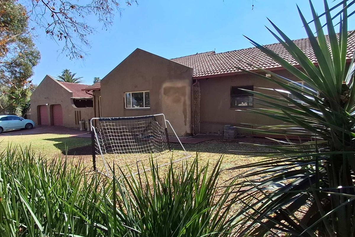 Rear view of the house featuring a tiled roof, lawn area, and a detached double garage with paved driveway access.