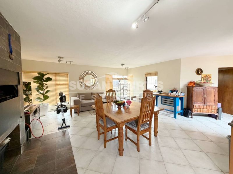 Spacious open-plan living and dining area featuring tiled flooring, a built-in fireplace, and ample natural light through large windows with venetian blinds.