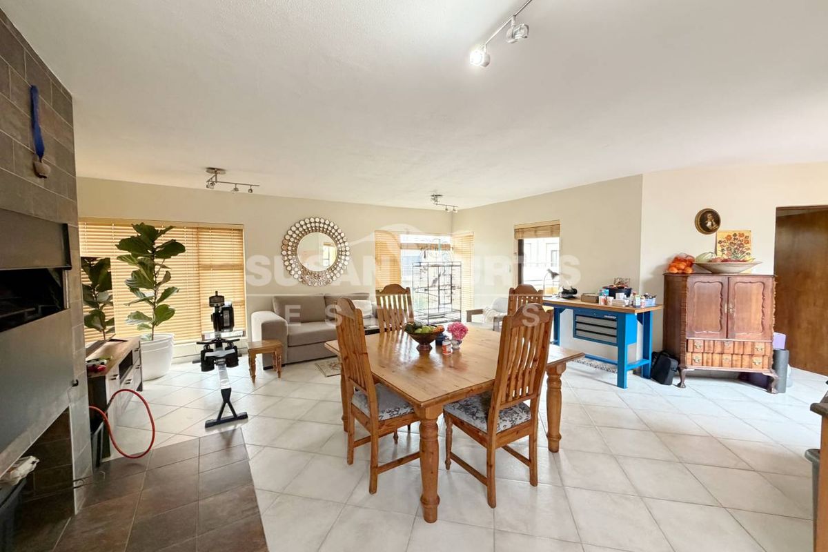 Spacious open-plan living and dining area featuring tiled flooring, a built-in fireplace, and ample natural light through large windows with venetian blinds.