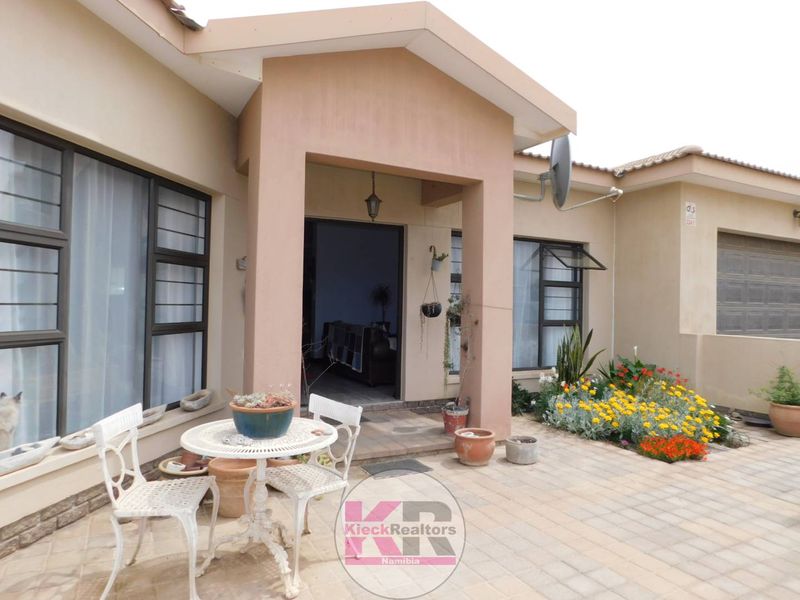 A rear exterior view featuring a paved patio area, covered entrance, and well-maintained garden beds adjacent to the house facade.
