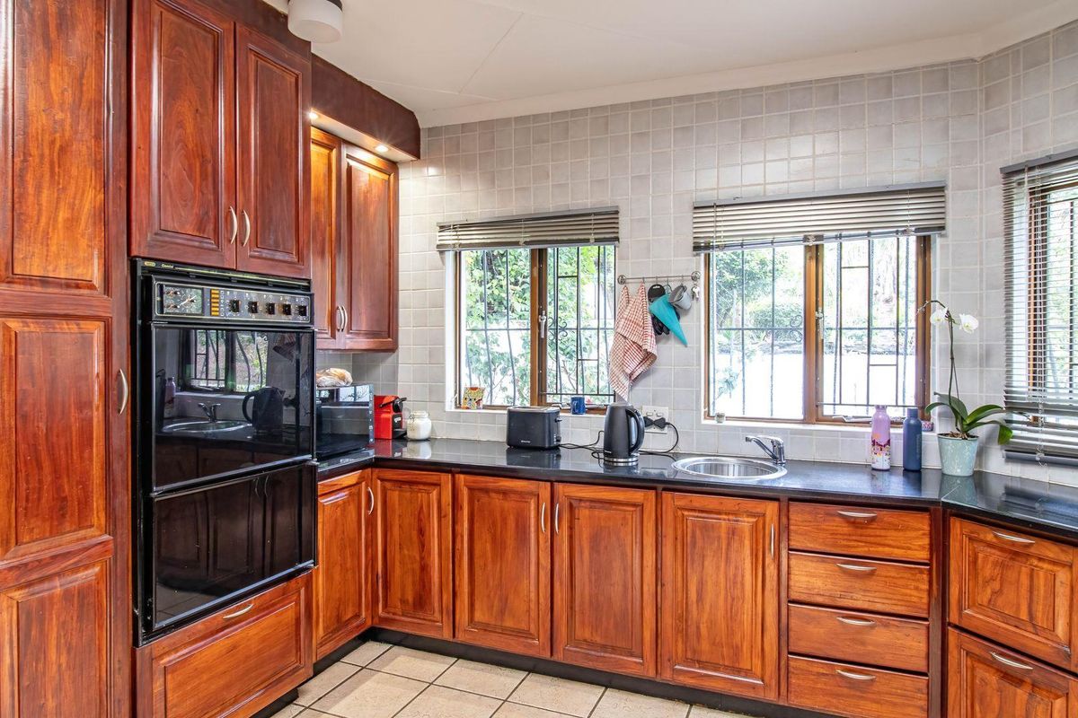 A functional kitchen featuring warm-toned wooden cabinetry, dark countertops, a built-in oven, and tiled backsplash with natural light from dual windows.