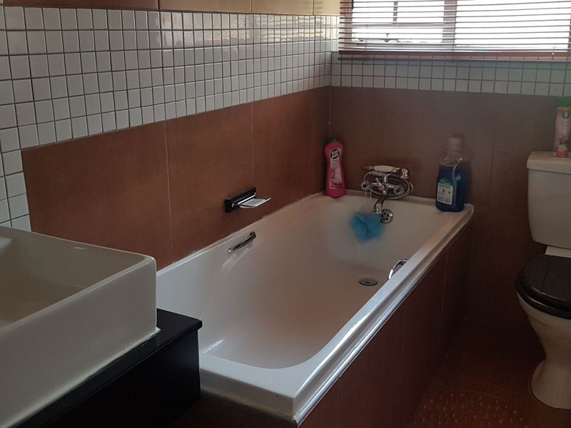 A functional bathroom featuring a bathtub, toilet, and basin with tiled wall finishes and window blinds.
