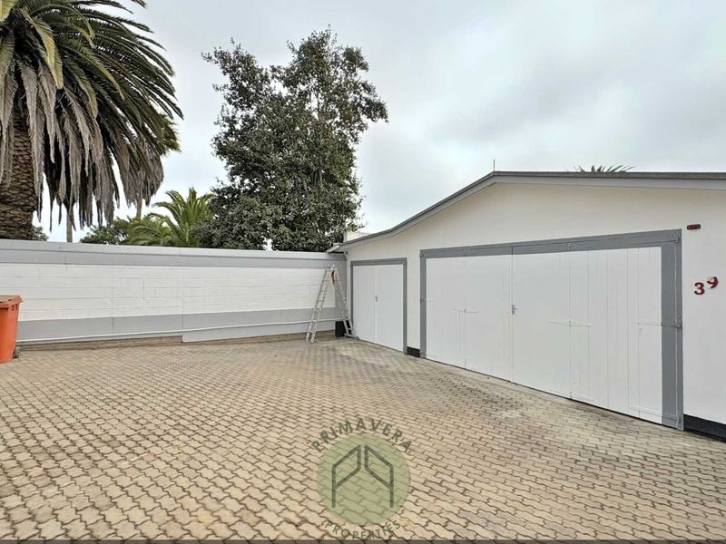 A paved driveway leading to a double garage with white doors and a surrounding boundary wall.