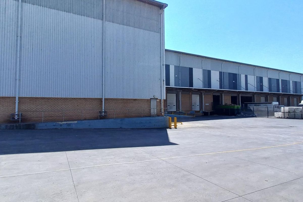 Industrial warehouse exterior featuring a large concrete hardstand area, multiple loading docks with roller shutter doors, and durable metal and brick facade construction.