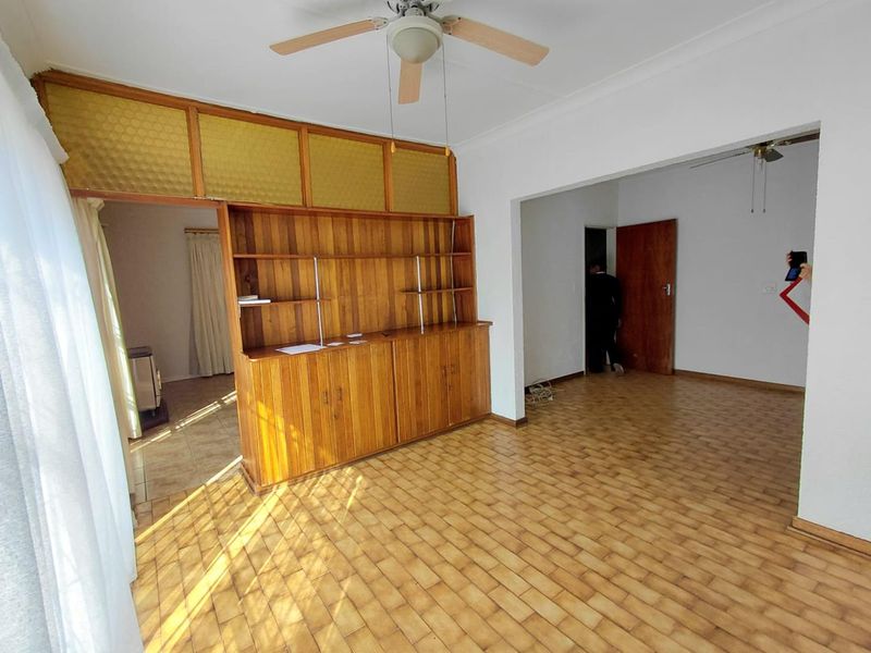 Spacious living area featuring original tiled flooring, built-in wooden cabinetry, and a ceiling fan, offering a blank canvas for modern updates.