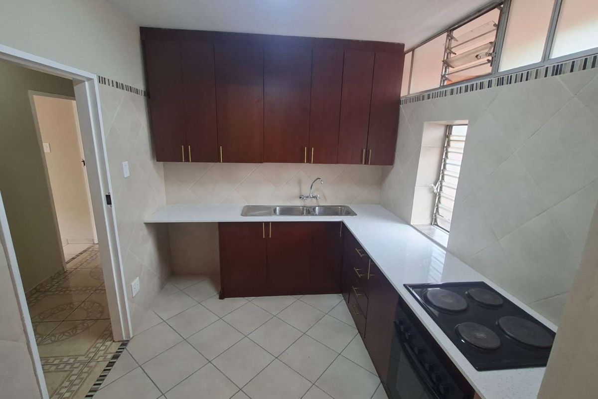 A clean, functional kitchen featuring dark wood cabinetry, white countertops, a built-in electric hob and oven, and tiled finishes throughout.