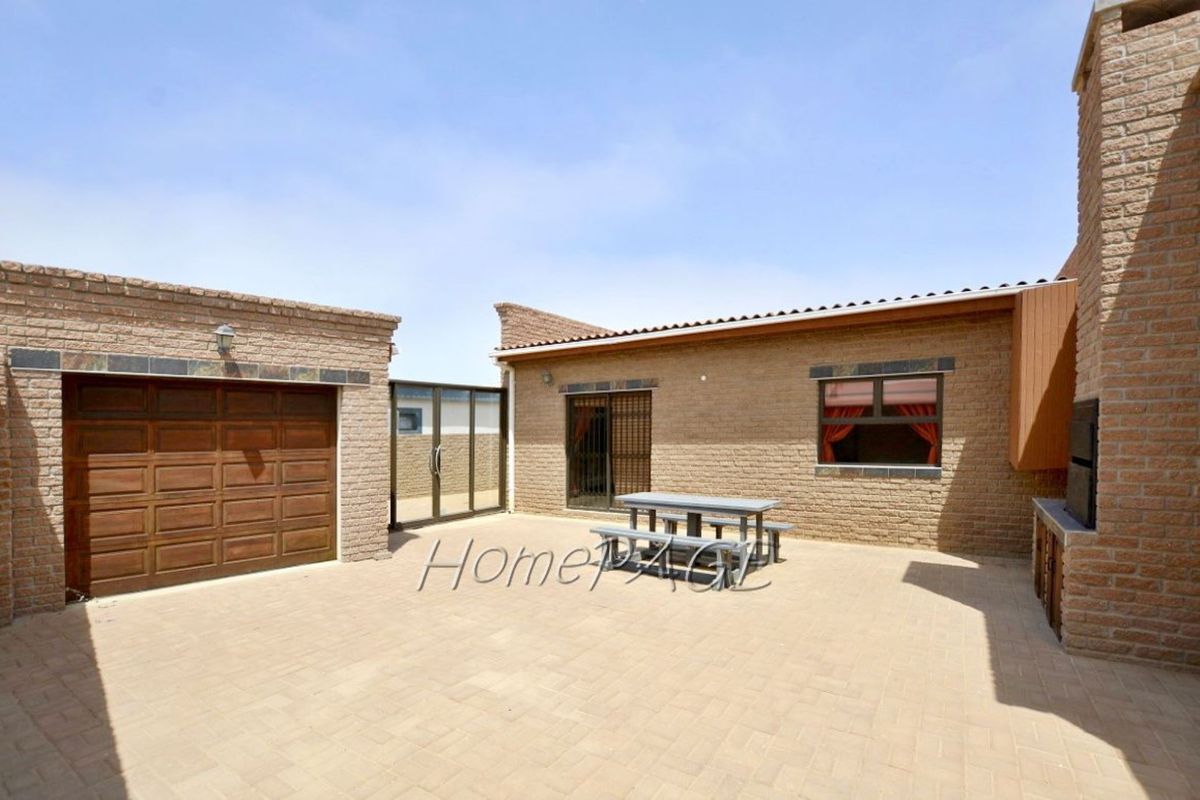 A paved rear courtyard featuring a built-in braai, brick exterior walls, a garage door, and sliding glass doors leading into the home.