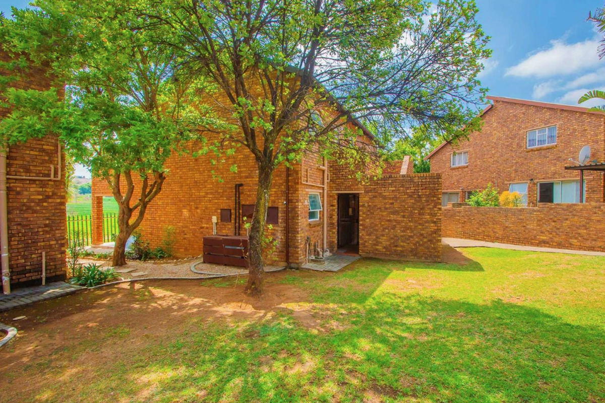 A view of the rear exterior of the apartment complex, featuring face brick construction, a well-maintained lawn, and mature trees.