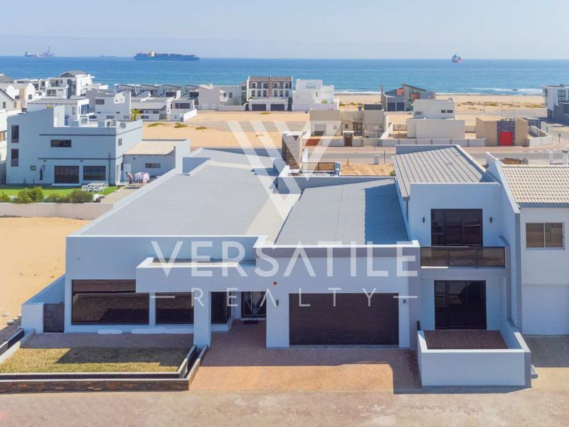 Aerial view of a modern coastal residence featuring a metal roof, paved driveway, and balcony, situated in a prime seaside location.