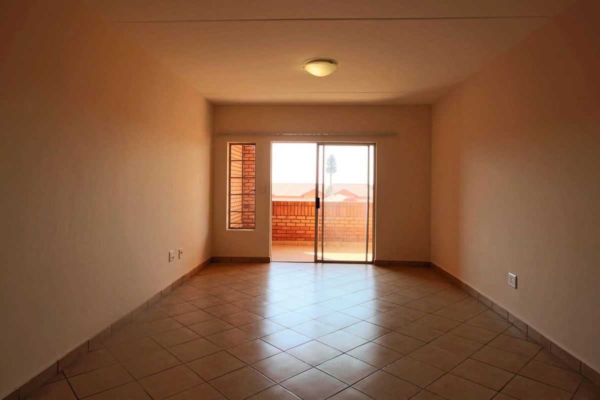 An empty, well-lit living room featuring tiled flooring and a sliding glass door that provides access to an outdoor balcony area.