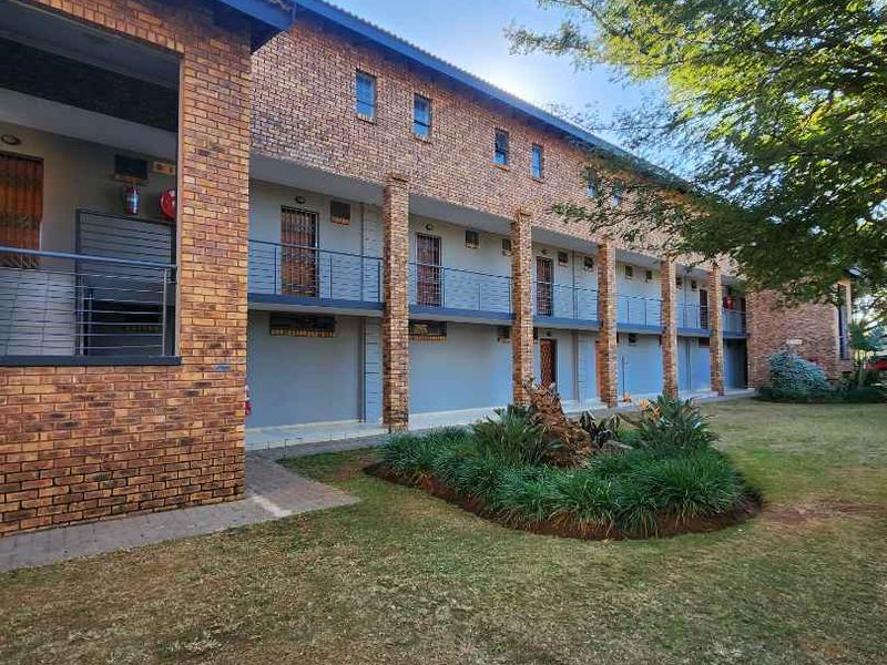 Exterior view of a multi-story apartment complex featuring face brick construction, metal balustrades, and a landscaped garden area.