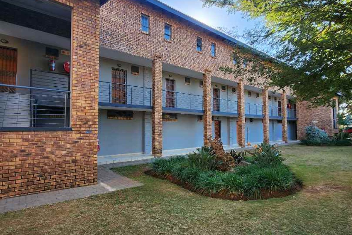 Exterior view of a multi-story apartment complex featuring face brick construction, metal balustrades, and a landscaped garden area.