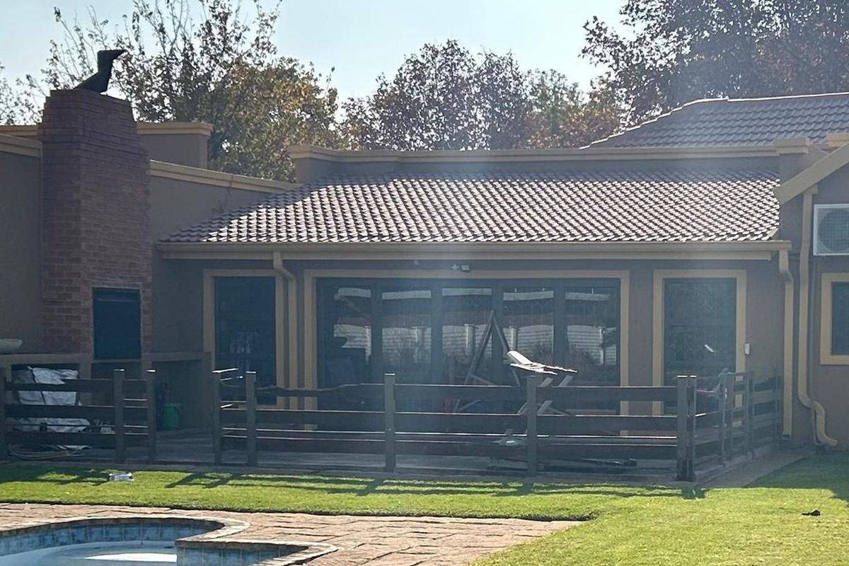 Rear view of the property featuring a covered patio area, outdoor brick fireplace, and a swimming pool set within a landscaped garden.