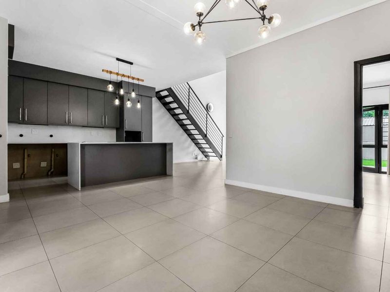 Spacious open-plan living and kitchen area featuring modern grey cabinetry, a central island, tiled floors, and a striking staircase with metal railings.