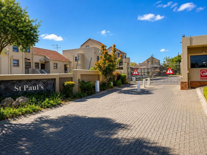 The entrance to St Paul's townhouse complex featuring a paved driveway, secure gated access, and a dedicated security guard house.