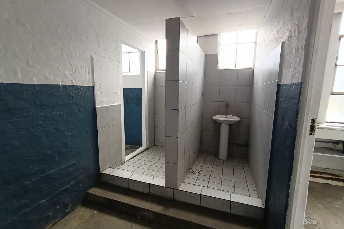 Industrial-style communal washroom area featuring tiled partitions, pedestal basins, and painted brick walls.