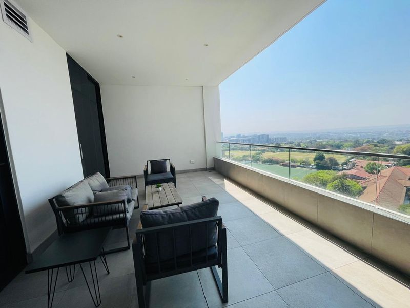 Spacious covered balcony featuring modern tiled flooring, a sleek glass balustrade, and expansive elevated views of the surrounding area.